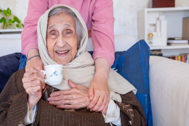 Kadın elleri kanepede kahve içerken büyükannesine sarılıyor.