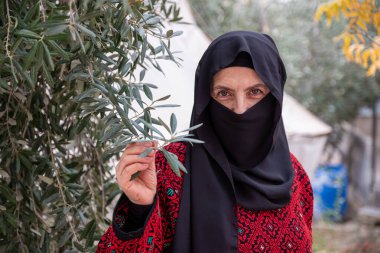 Mülteci kampında zeytin ağacının arkasında geleneksel giysiler giyen kadın portresi