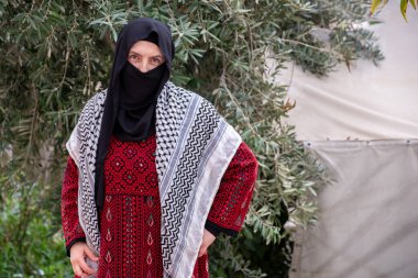 Mülteci kampında zeytin ağacının arkasında geleneksel giysiler giyen kadın portresi