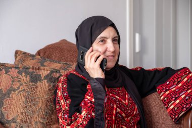 Filistin 'de geleneksel giysiler giyen bir kadın Filistin' deki akrabalarıyla kanepede telefon görüşmesi yapıyor.