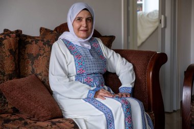 Geleneksel kıyafetler giyen yaşlı kadın yüzünde gülümsemeyle kanepede oturuyor.