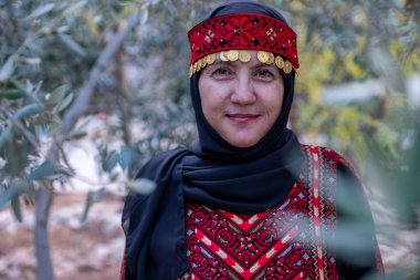 Zeytin ağaçlarında geleneksel giysiler giymiş bir kadının portresi elinde bir dalla yüzünde gülümsemeyle