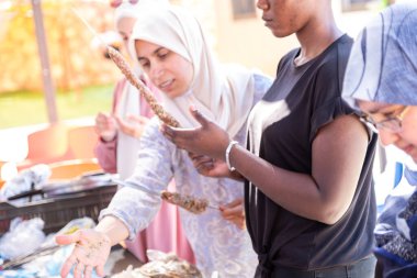Çok ırklı insanlar piknikte ve kebap ve barbekü hazırlarken birbirlerine yardım ediyorlar.