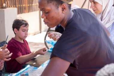 Çok ırklı insanlar piknikte ve kebap ve barbekü hazırlarken birbirlerine yardım ediyorlar.