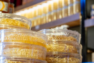 Balmumuyla balmumu kaplı balmumu plastik kutunun içinde rafın arka planı bal kavanozlarıyla dolu.