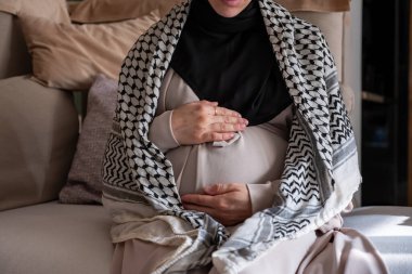 Filistinli hamile kadın kanepede keffiyeh giyiyor.