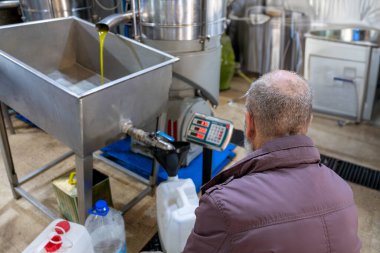 Yaşlı bir Müslüman için en üst görünüm, taze zeytinyağını bir huni ve baskı yapan bir fabrikadaki tartıyı kullanarak plastik galonlara doldurma işlemidir.