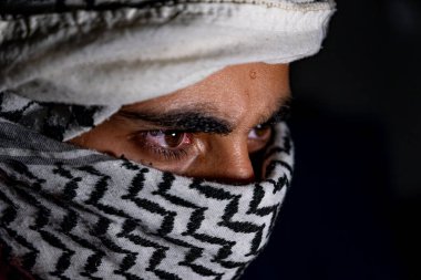 Siyah arka planda beyaz keffiyeh giyen Pearl 'ün portresi. Şiddet ve işgale karşı olduğu için gözlerinde öfke ifadesi var.