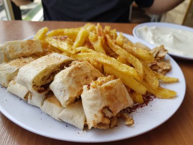 Shawarma tabağı ahşap masada servis ediliyor. Yakın çekim ve üst manzara. Ayrıca sarımsak kabının yanında patates kızartması da var.