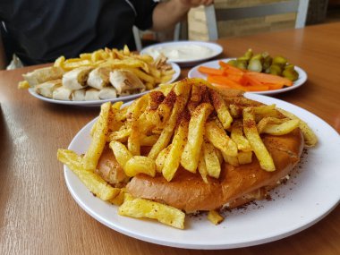 Shawarma tabağı ahşap masada servis ediliyor. Yakın çekim ve üst manzara. Ayrıca sarımsak kabının yanında patates kızartması da var.