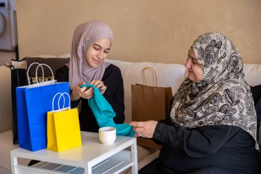 Arap kadının annesine hediye etmesi ve alışveriş yaptıktan sonra yeni kıyafetlerini oturma odasında poşetlerle göstermesi.