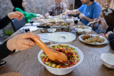 Karısı, büyük bir ailenin ortak masasında öğle yemeği sırasında misafirlere ihtiyaçlarını karşılamak için yanına büyük bir kase yoğurt koyar..