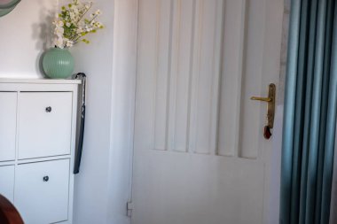 Modern iç tasarımı modern dairede olan minimalist koridor. Beyaz duvardaki yeşil çerçeve aynasının yanında rahat bir ayakkabı deposu. Göğüs çekmeceleri ve yeşil perdeleri var.