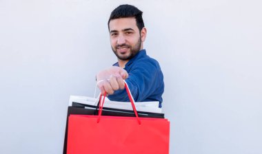 Beyaz arka planda alışveriş torbaları taşıyan genç bir erkek. Neşeli yüzlü, siyah beyaz cuma terfileri için.