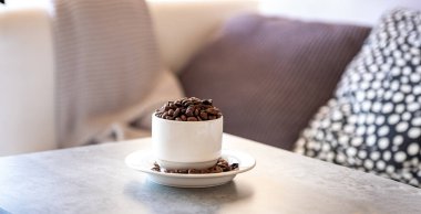 Kahve çekirdeği dolu kahve fincanı gri oturma odasındaki kanepede.