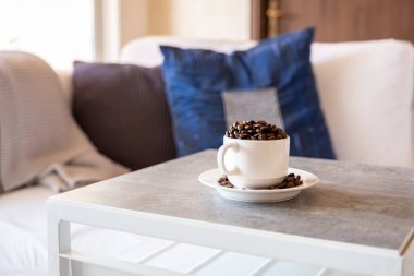 Arka planda kitap ve kanepe olan gri oturma odası masasında bir fincan kahve.