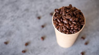 Gri arkaplanlı kahve çekirdekleri ile dolu bir fincan kağıt kahve.