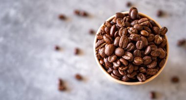 Gri arkaplanlı kahve çekirdekleri ile dolu bir fincan kağıt kahve.