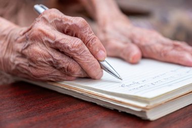 Yaşlı birinin not defterine notlar yazması için buruşuk eller.
