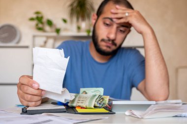 Genç sakallı erkek oturma odasında yaşam masraflarını hesaplıyor.