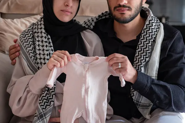 Stock image Husband and his wife holding newborn clothes for there dead child  while wearing palestinian keffiyeh in living room