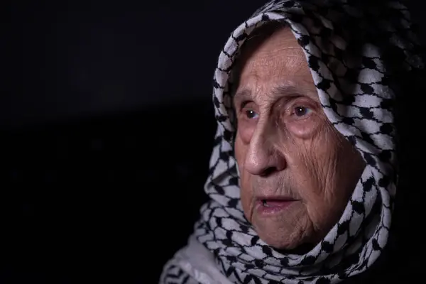 stock image portrait of an old lady in dark background wearing white palestinian keffiyeh with smile on her face looking for freedom and hope to Right of Return for Palestinians