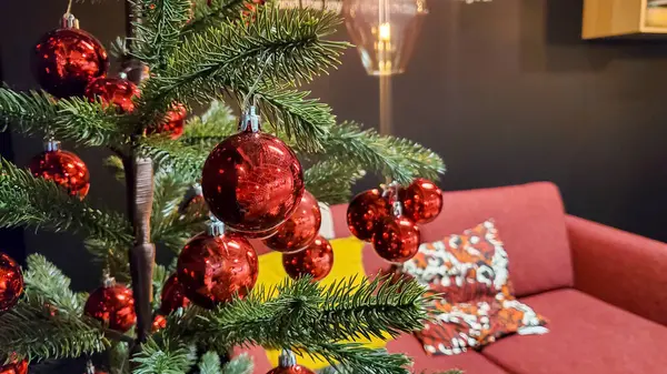 Oturma odasında kırmızı süslemeli Noel ağacı, rahat kanepe ve minderler.