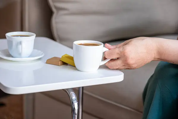 stock image Old lady hand holding white cup of coffee with chocolate pieces have gold on her wrist with shiny background