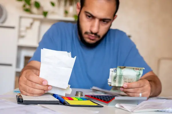 Genç sakallı erkek oturma odasında yaşam masraflarını hesaplıyor.
