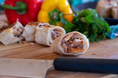 Shawarma parçaları siyah tabakta, tahta masada, arka planda tatlı biberler ve bıçakla.