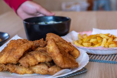 İnsan eli, masada patates kızartmalı tavuk filetosu ve yenmesi için sos.