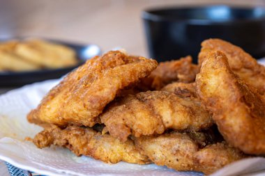 Tahta masada kızarmış tavuk filetosu patates kızartması, sos ve soğan halkaları ile servis ediliyor.