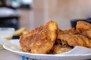 Tahta masada kızarmış tavuk filetosu patates kızartması, sos ve soğan halkaları ile servis ediliyor.