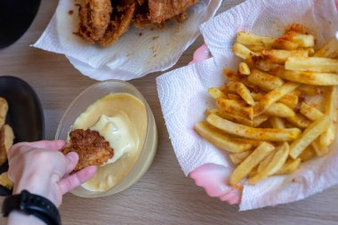 İnsan eli, masada patates kızartmalı tavuk filetosu ve yenmesi için sos.