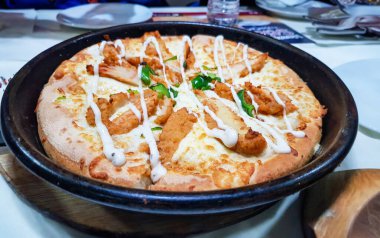 Alfredo sosu pIzza siyah tabakta beyaz masada servis edilir.