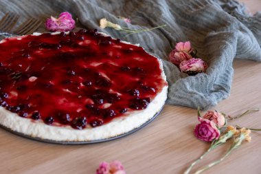 Çevresinde kiraz jölesi ve güller olan soğuk bir cheesecake, ahşap arka planda servis edilir. Yeşil fırlatma ve antika çatallarla.