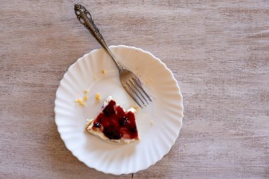 Çatallı, çiçekli ve yeşil peçeli ahşap masada servis edilen vişneli soğuk cheesecake.