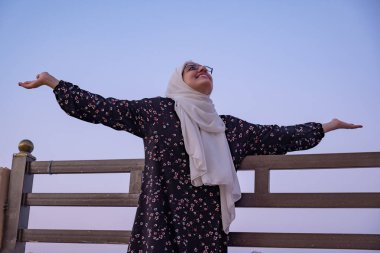 female wearing hijab and islamic wears having vacation in resort with smile on their face and beautiful blurred lights in the background clipart