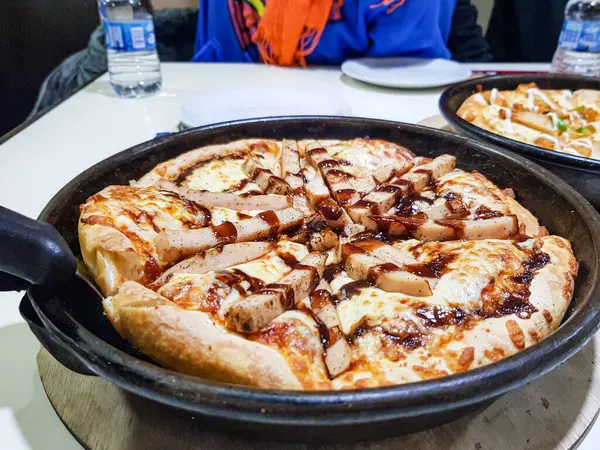 Izgara tavuk pIzza servis edilir siyah tabak üzerinde beyaz masa etrafında insanlar