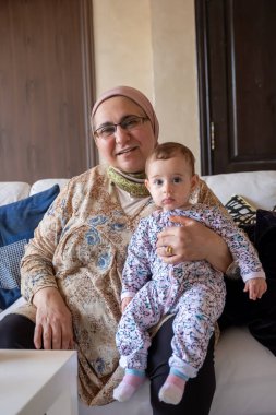 Sıcak oturma odasında, bir büyükanne torununa neşeyle sarılır, hayatlarının bu güzel anında hem heyecan hem de aşk saçar.