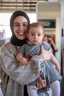 Yeni doğmuş bebeğini kucağında tutan bir kadın için dikey fotoğraf. Kameraya neşeli ve iyi giyimli bir şekilde bakıyor. İlk kutlama ve aile anları için.