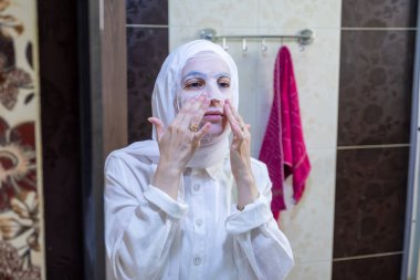 Yüzüne bakıp gülümseyen, kaplıcaya yüz maskesi takan Arap Müslüman kadın.