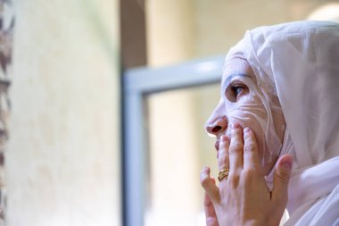 Yüzüne bakıp gülümseyen, kaplıcaya yüz maskesi takan Arap Müslüman kadın.