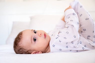 Küçük sevimli beyaz bebek evde yatakta yatarken eğleniyor, sevimli Arap kız burada ayak parmaklarıyla oynuyor ve yatak odasında dinlenirken gülüyor, üst görünüm, kopyalama alanı