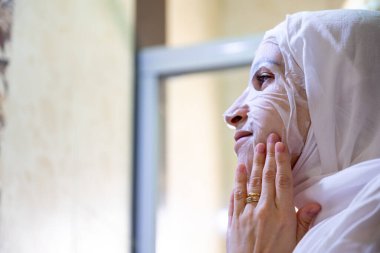 Yüzüne bakıp gülümseyen, kaplıcaya yüz maskesi takan Arap Müslüman kadın.