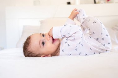 Yıldız desenli pijamalarıyla beyaz bir yatakta uzanmış, gülümseyen ve şakacı sevimli bir bebek. Çocukluk sevincini ve masumiyetini vurgulayan fotoğraflar için mükemmel..