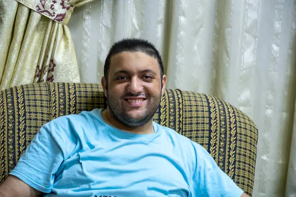 stock image Man in glasses, smiling and relaxed at home, captured in candid portraits. Sitting on an armchair, wearing casual shirts. Perfect for lifestyle and everyday moments themes