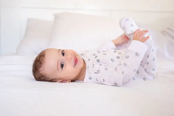 stock image Cute Funny Little white Baby Having Fun While Lying On Bed At Home, Adorable arabian  Infant girl Playing With here Toes And Laughing While Resting In Bedroom, Top View, Copy Space