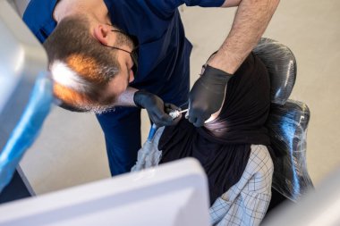 Klinikteki tıbbi ekipmanlarla hastayı muayene eden dişçi.