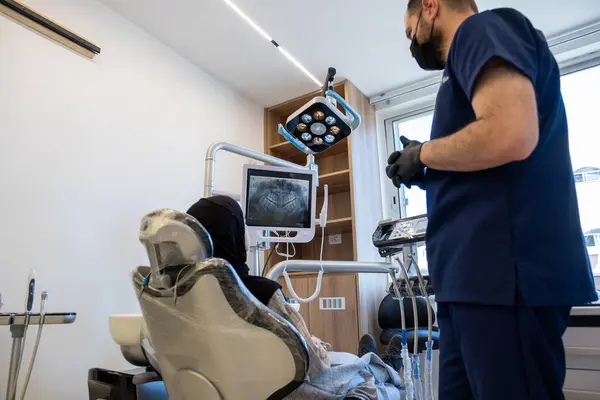 stock image Conversation between dentist and muslim female wearing hijab looking at her tooths x-ray scan on the screen and the doctor is describing her treatment plan to avoid such illness and toothache again